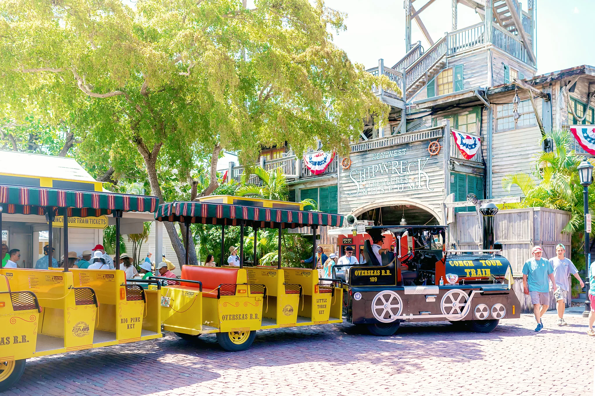 Photo of Key West Conch Train in front of the shipwreck museum. The train is yellow and open air.