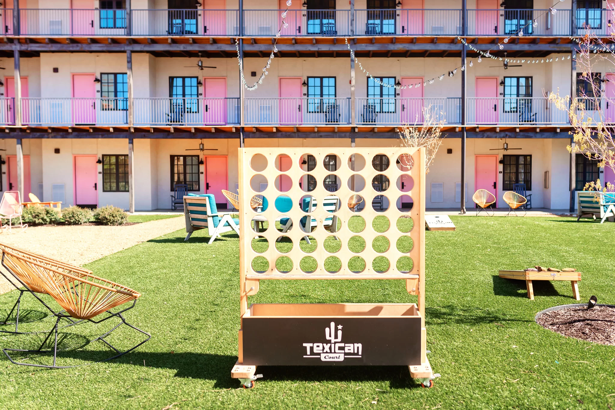 A giant tick tack toe game in a green courtyard at the Texican Ranch Hotel. You can see three stories of the hotel with pink doors in the background.