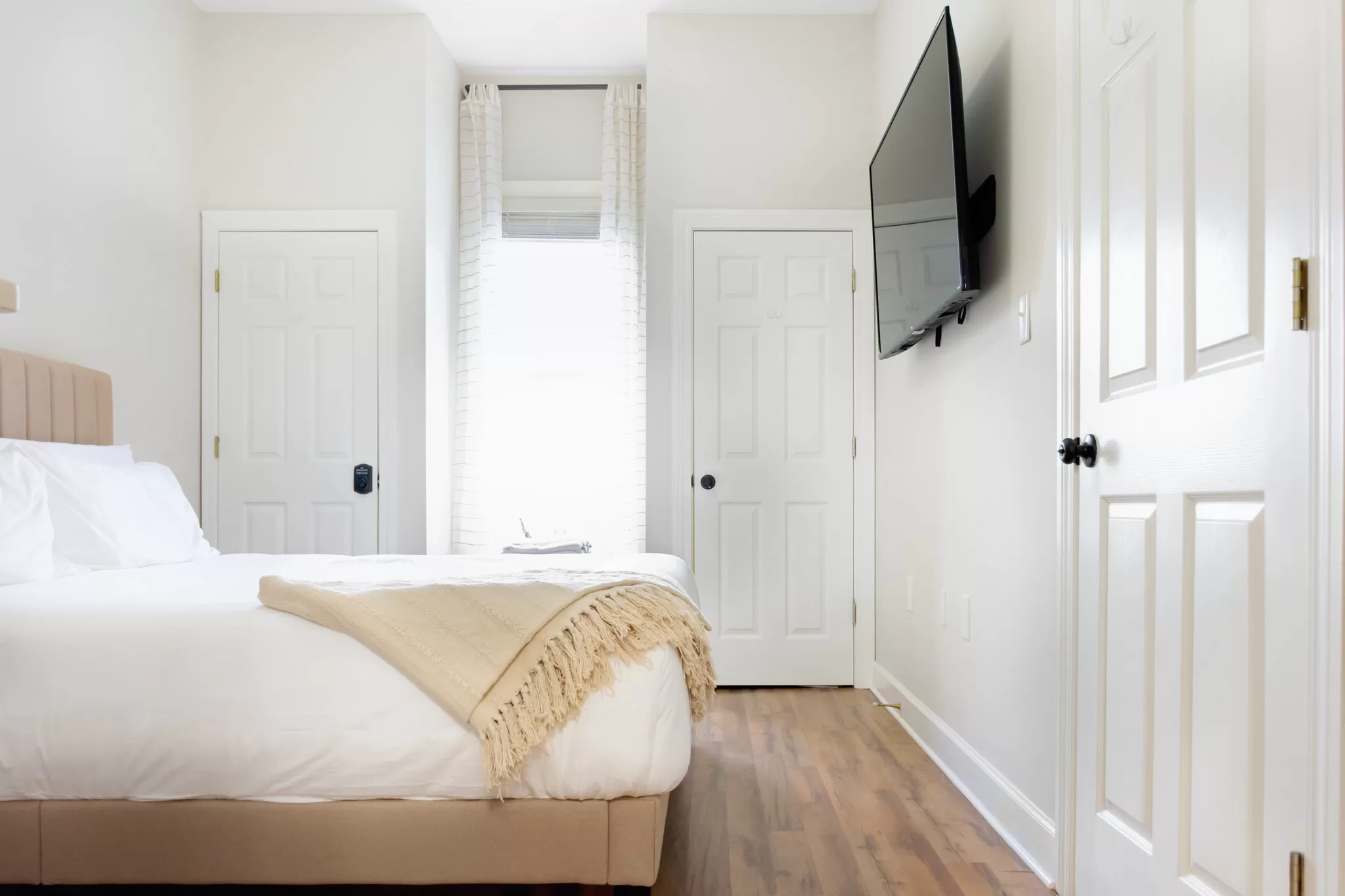 A photo showing a bedroom in an Airbnb.  Hooks are on the back of the doors and the walls are painted white. 