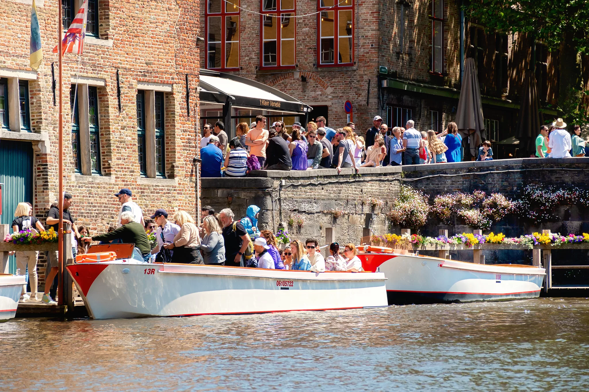 People lined up for a canal tour in Bruges.  The boat is white with red trim.