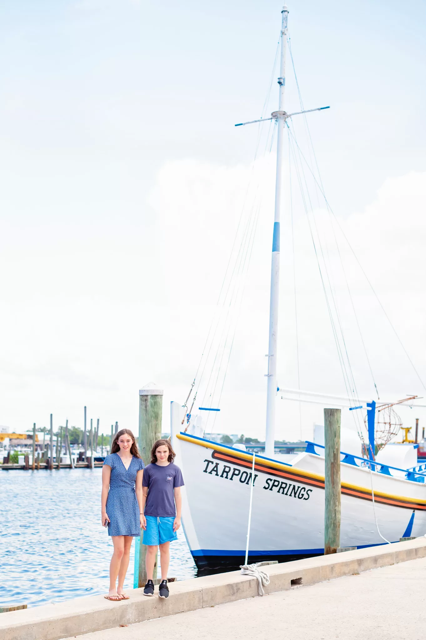 This image is for a blog post about Tarpon Springs Florida and shows two kids standing next to a sponge boat that says Tarpon Springs on it. The kids are wearing blue and it's a sunny day.