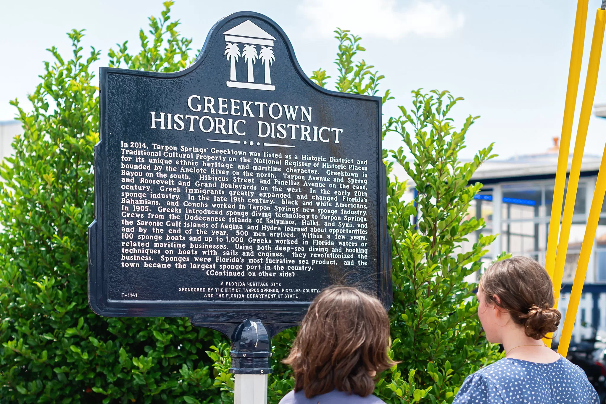 This image is for a blog post about Tarpon Springs Greek History and shows two kids looking at a Florida historic marker sign and reading it. 