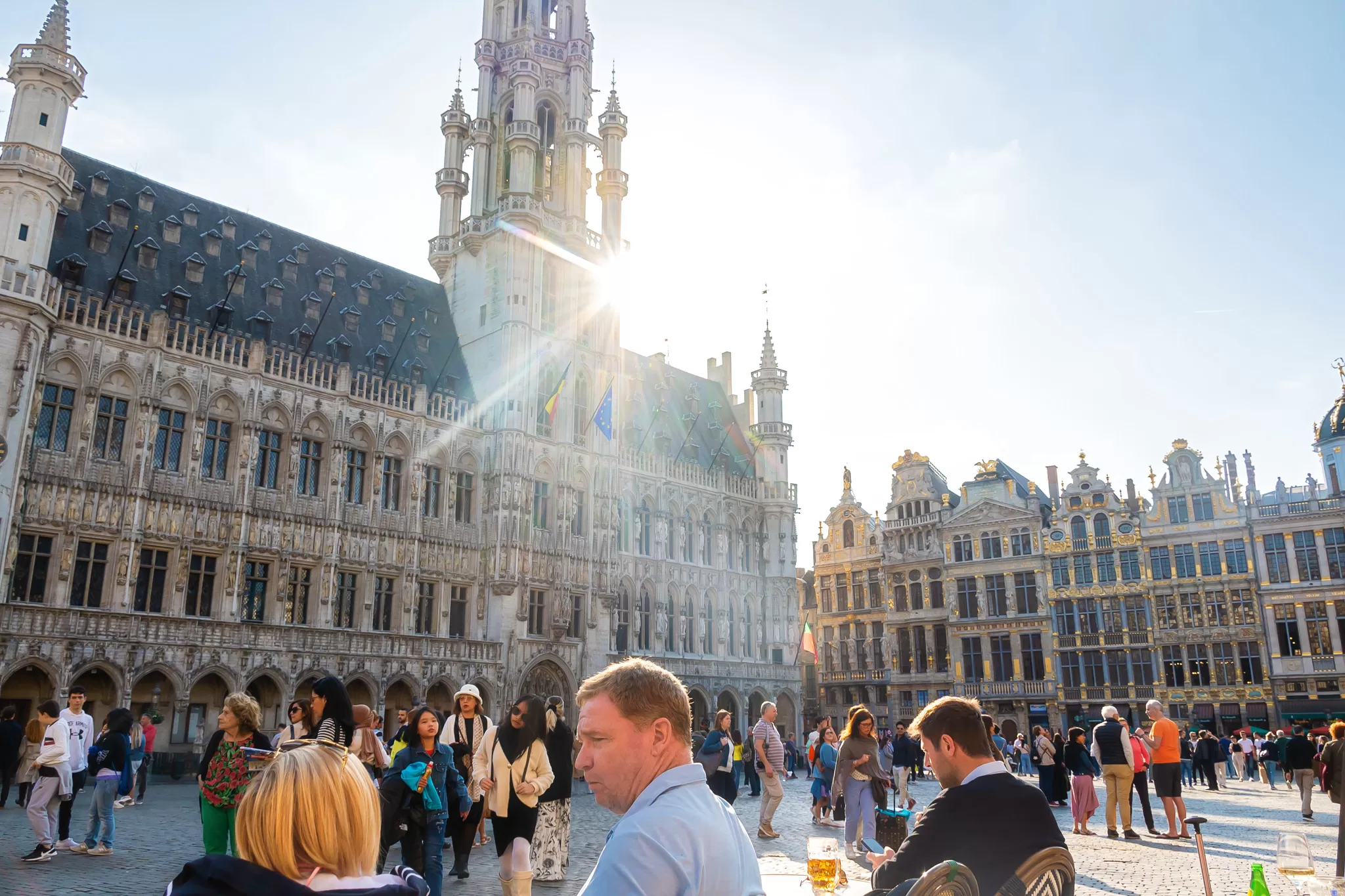 This image shows the crowds on a summer day at Grand Place in Brussels, Belgium.  Historic guilded buildings are in the background. 