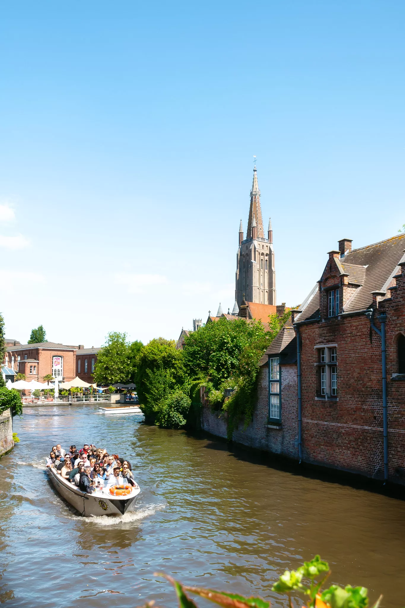 The Canals in Bruges with a canal tour boat full of people about to go under a bridge.