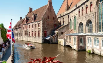 A canal tour boat in Bruges cruises along the water with historical buildings in the background.