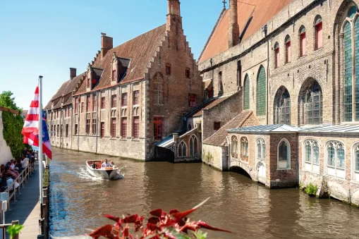 A canal tour boat in Bruges cruises along the water with historical buildings in the background.