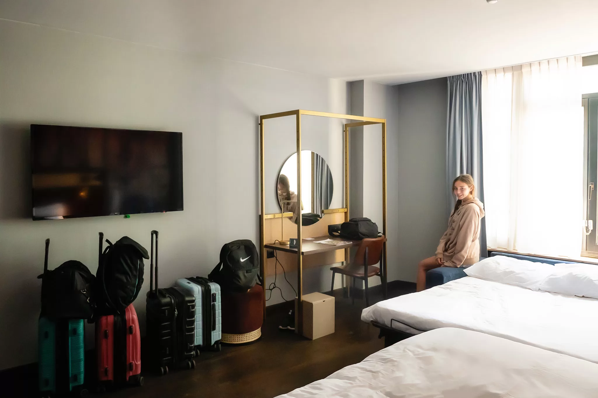 A girl sitting on the bed the Hotel Indigo Brussels City in Belgium Europe. 4 Carry on luggage bags are shown.