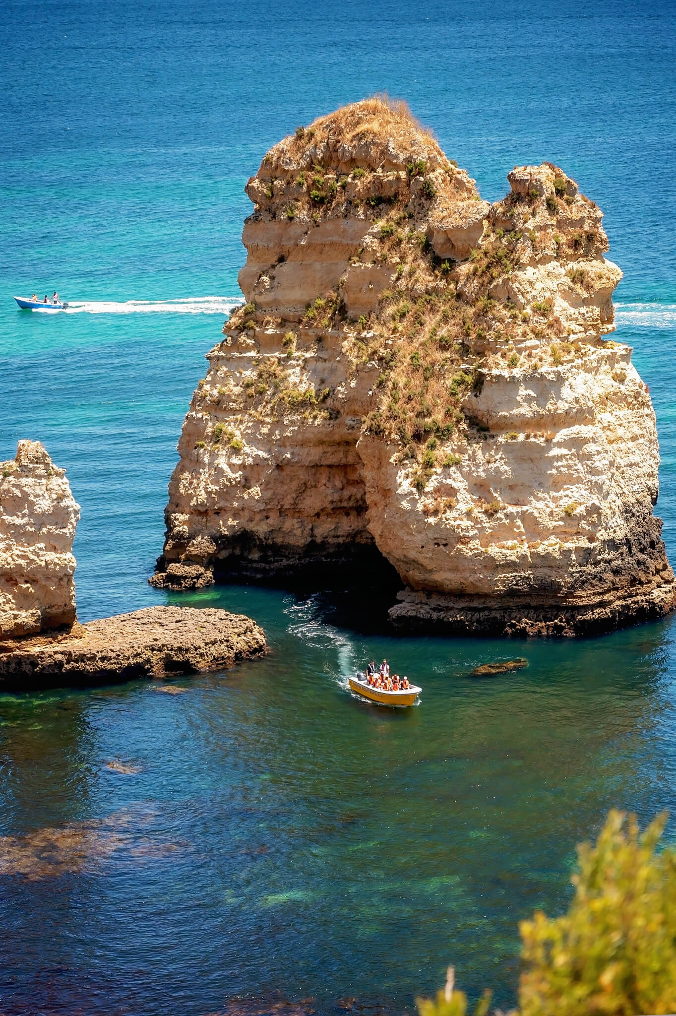Tall limestone sea stack rising from clear blue water, with a small boat nearby carrying passengers.