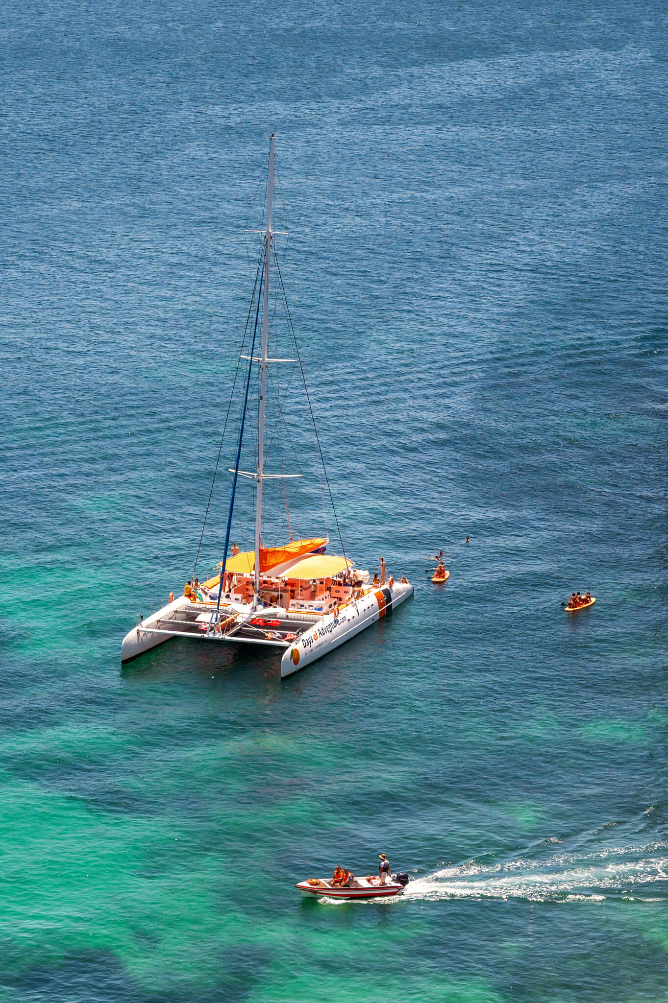 Lagos Portugal Algarve Summer Trip 49 • Our Little Lifestyle Catamaran with orange canopy anchored in clear turquoise water, with people nearby and a small motor boat in front.