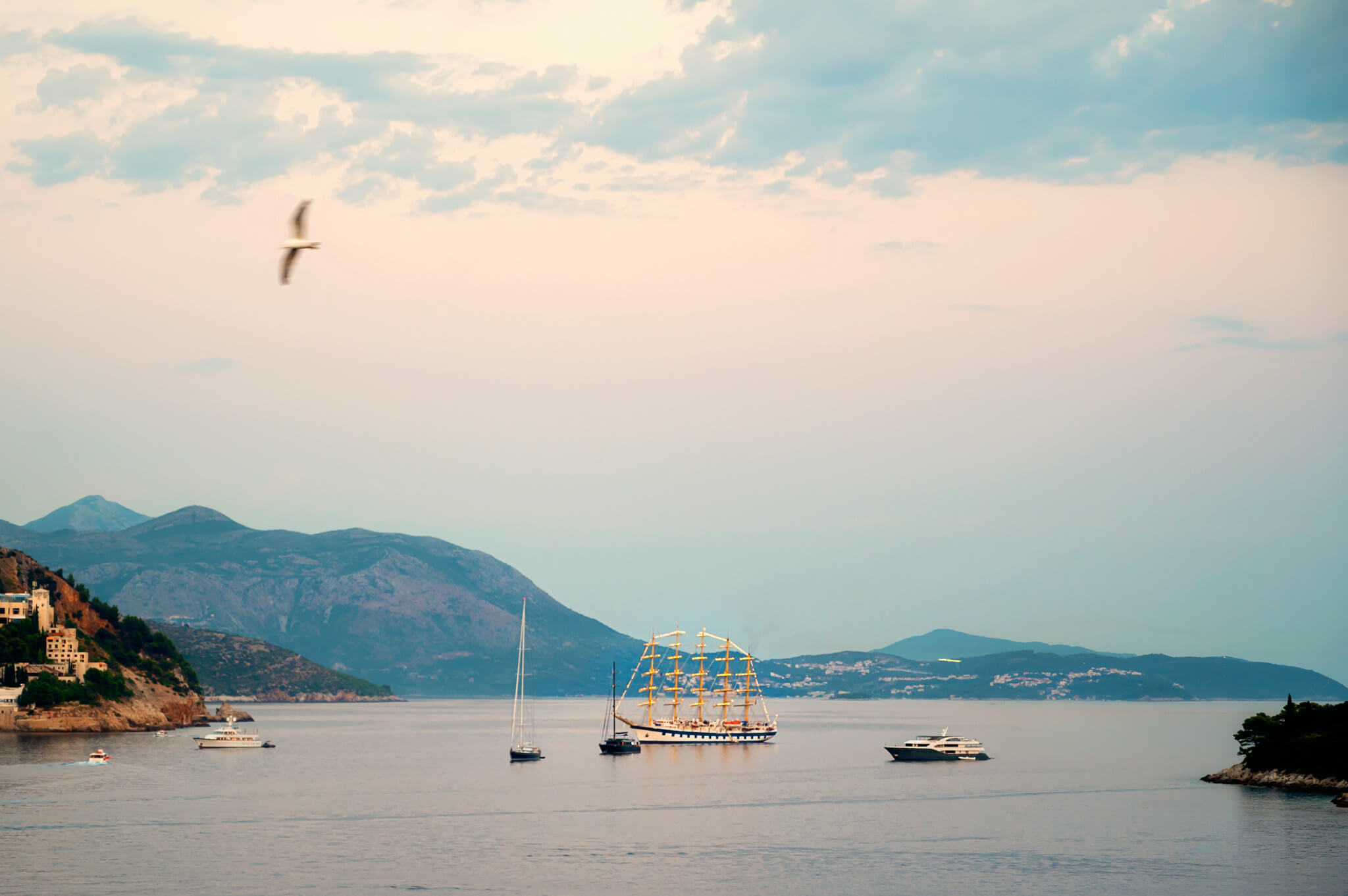 Three-masted Royal Clipper sailing ship anchored in a calm bay, with distant hills and small boats nearby under a pastel sky in Dubrovnik Croatia