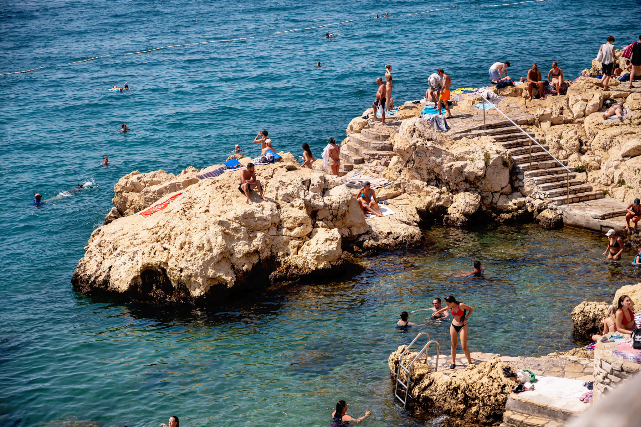 People sunbathing and swimming on a rocky coastline beside clear blue water under sunny skies Star Clippers Royal Clipper Day 6 Rovinj Croatia