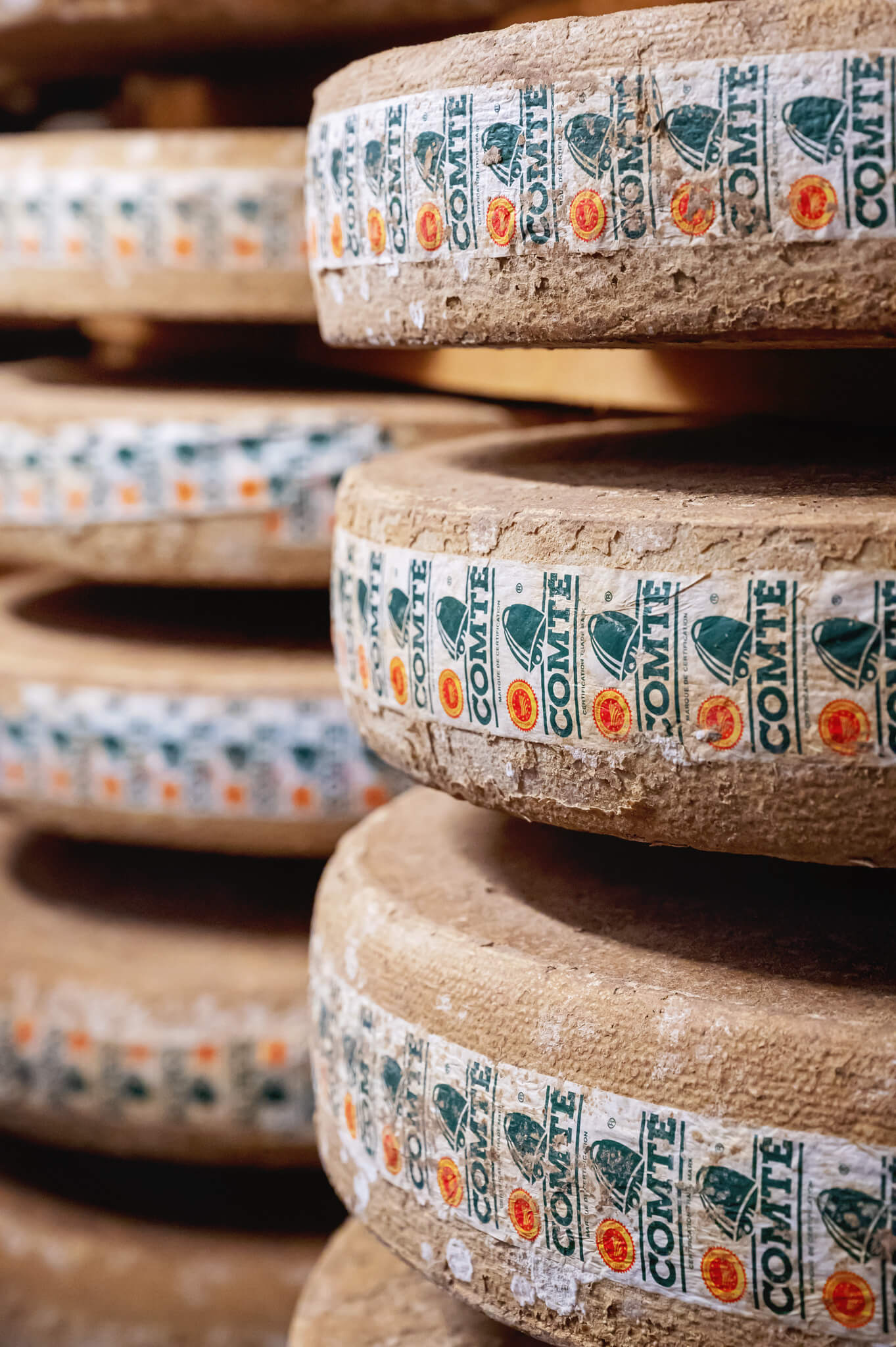 Stack of round Comté cheese wheels wrapped in branded paper, showing rind cracks/texture.