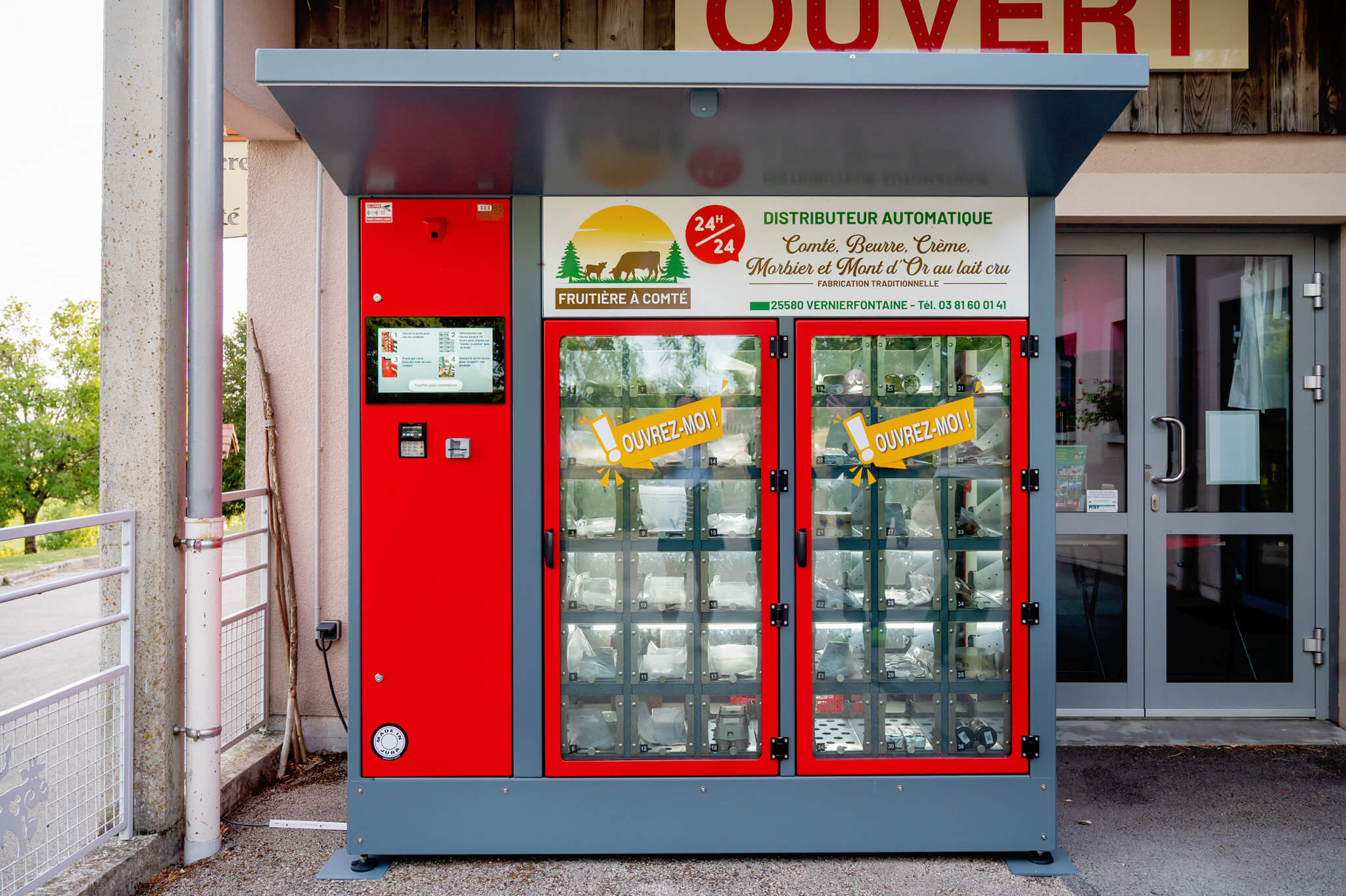 Automated cheese vending machine with red compartments and a sign reading'Distributeur Automatique' with 'Comté' branding outside a shop.