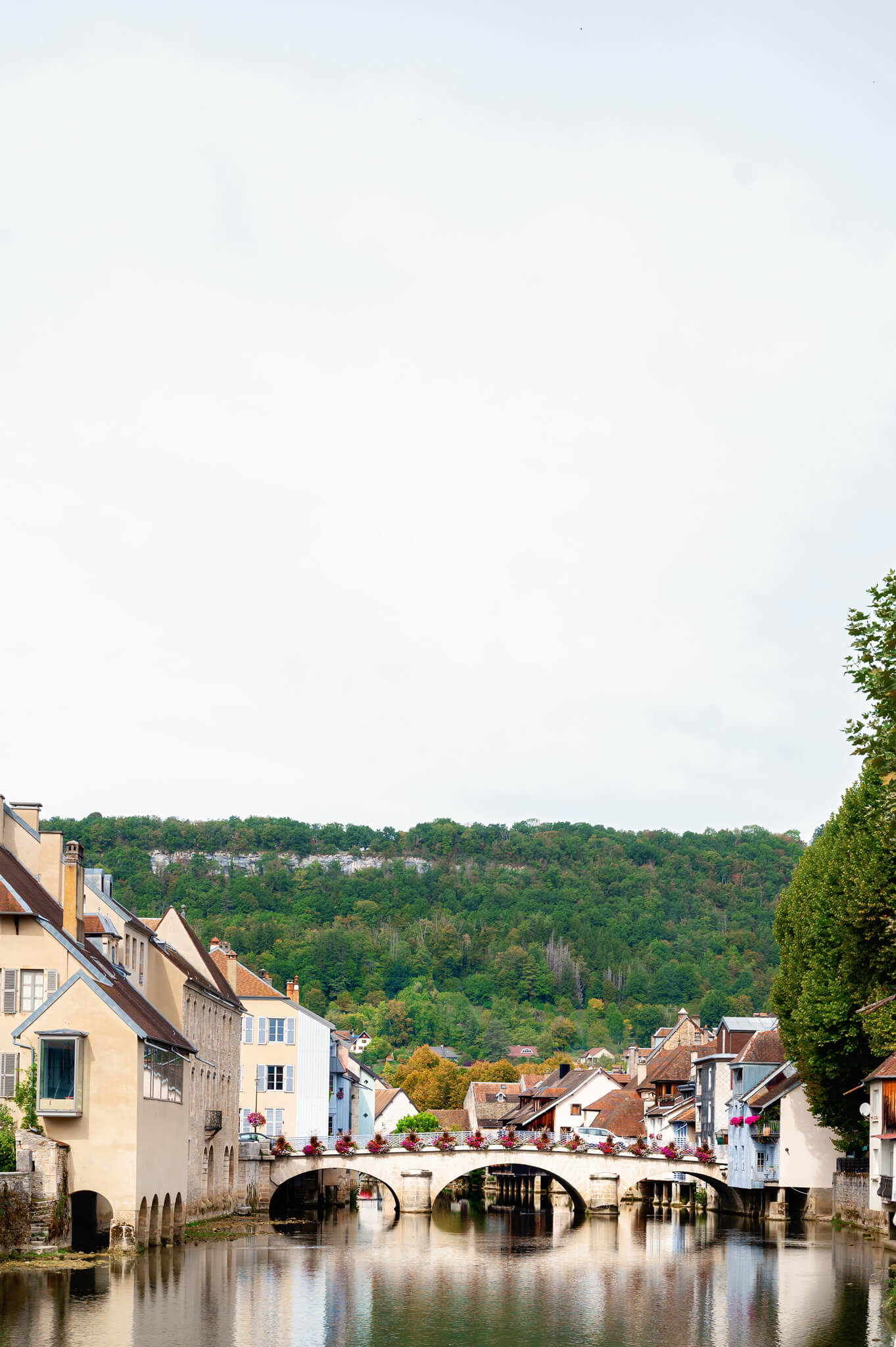 Ornans, France Colorful French village by a calm river with a stone arched bridge and pastel houses lining the water’s edge