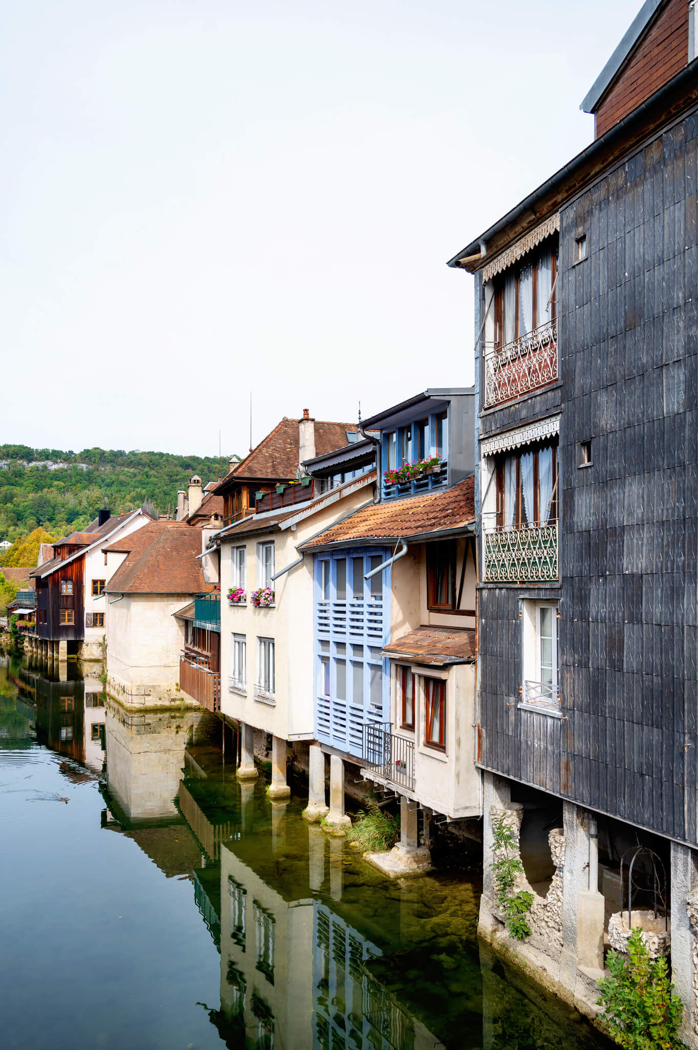 Ornans, France Row houses with wooden balconies along a calm canal, built on stilts and reflecting in the water.