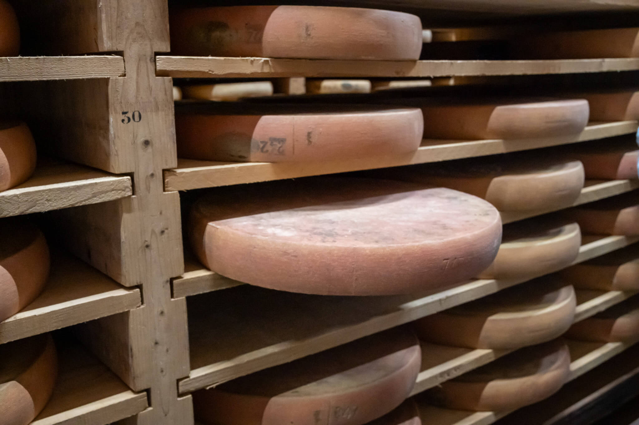 Rows of large circular comte cheese wheels resting on wooden racks in a dairy aging cellar.